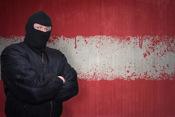 Uomo pericoloso in maschera in piedi vicino a un muro con bandiera nazionale dipinta di austria — Foto Stock