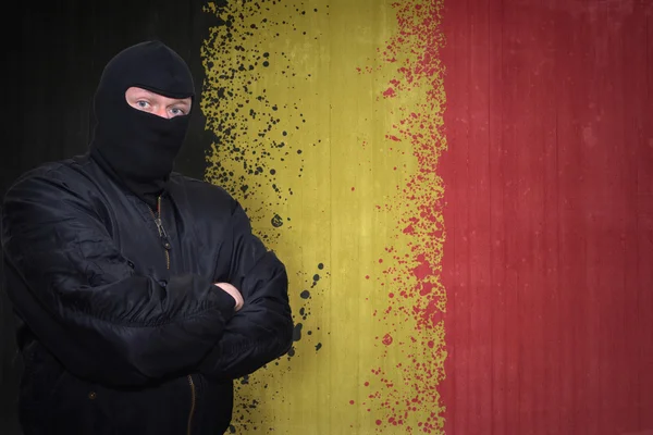Hombre peligroso en una máscara de pie cerca de una pared con la bandera nacional pintada de Bélgica — Foto de Stock