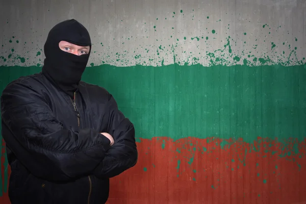 Hombre peligroso en una máscara de pie cerca de una pared con la bandera nacional pintada de bulgaria — Foto de Stock