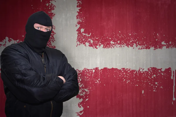 Homem perigoso em uma máscara que está perto de uma parede com bandeira nacional pintada de denmark — Fotografia de Stock