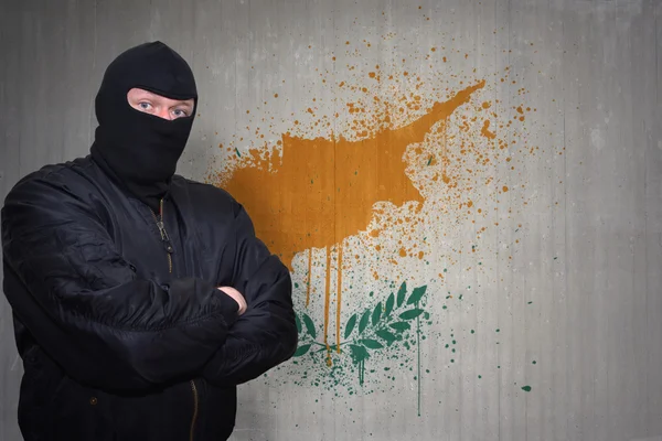 Uomo pericoloso in una maschera in piedi vicino a un muro con bandiera nazionale dipinta di Cipro — Foto Stock