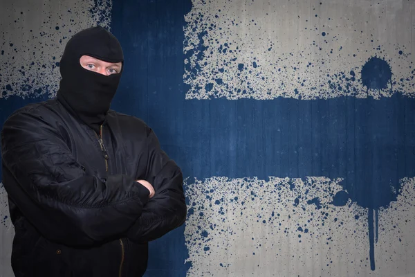 Farlig man i en mask stående nära en mur med målade nationella flaggan i Finland — Stockfoto