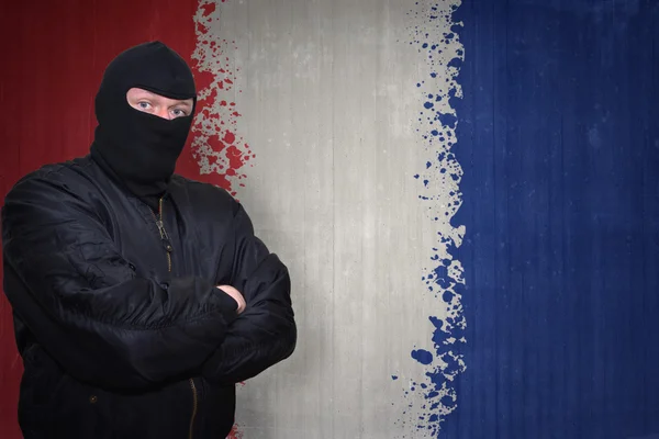 Niebezpieczny człowiek w masce stojącej w pobliżu ściany z malowaną narodową flagą Francji — Zdjęcie stockowe