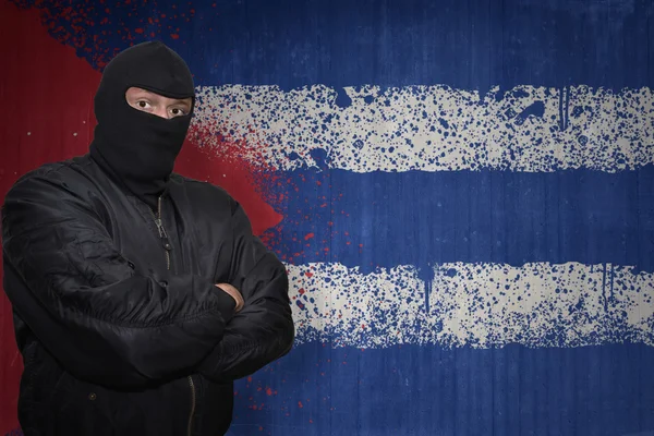 Hombre peligroso en una máscara de pie cerca de una pared con la bandera nacional pintada de Cuba — Foto de Stock