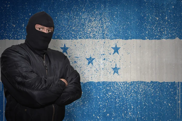 Uomo pericoloso in una maschera in piedi vicino a un muro con bandiera nazionale dipinta di honduras — Foto Stock