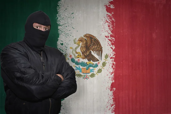 Homem perigoso em uma máscara de pé perto de uma parede com pintado bandeira nacional do méxico — Fotografia de Stock