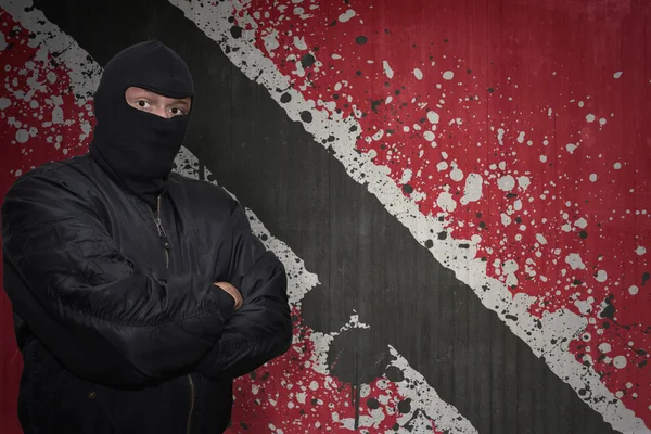 Homem perigoso em uma máscara que está perto de uma parede com a bandeira nacional pintada de trinidad e tobago — Fotografia de Stock