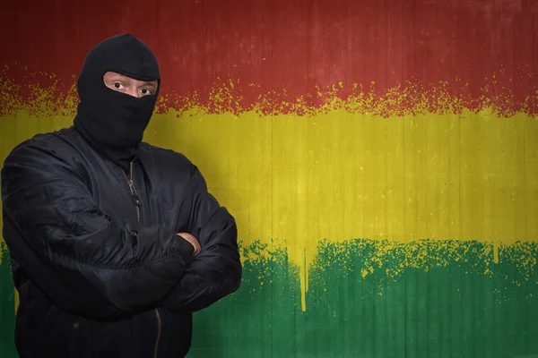 Hombre peligroso en una máscara de pie cerca de una pared con la bandera nacional pintada de Bolivia — Foto de Stock