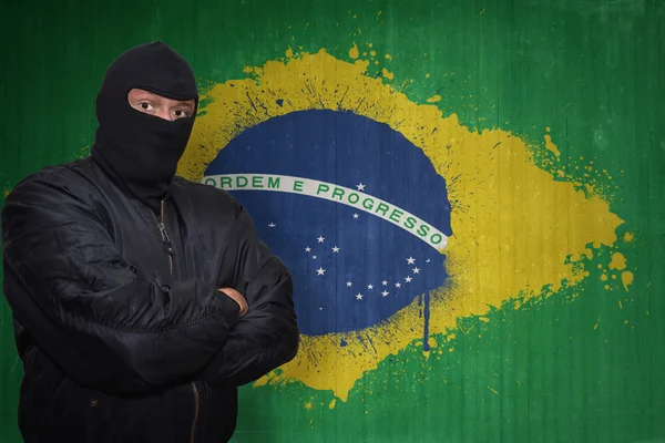 Dangerous man in a mask standing near a wall with painted national flag of brazil — 图库照片
