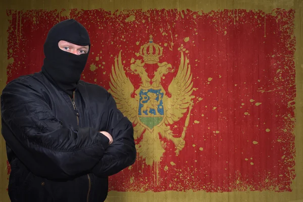 Nebezpečný muž v masce stojící u zdi s pomalovanou národní vlajkou Černé hory — Stock fotografie