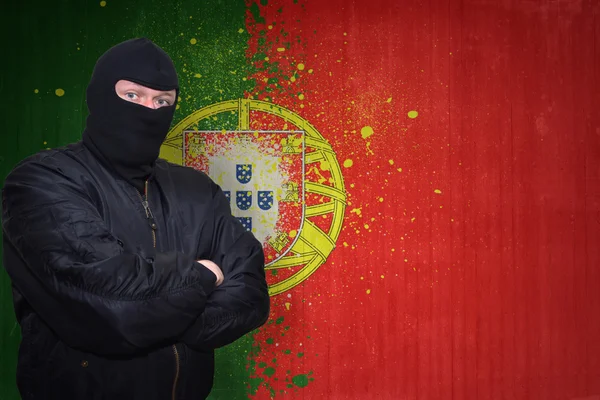 Uomo pericoloso in una maschera in piedi vicino a un muro con bandiera nazionale dipinta del Portogallo — Foto Stock