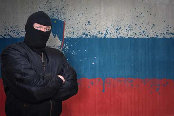 Dangerous man in a mask standing near a wall with painted national flag of slovenia — Stock Photo, Image