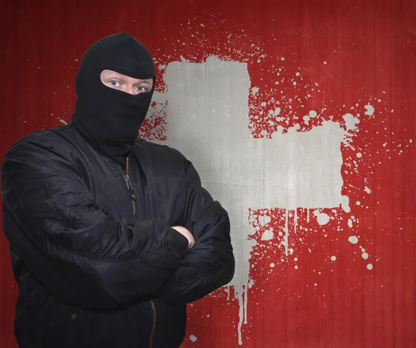 Farlig man i en mask stående nära en mur med målade nationella flaggan i Schweiz — Stockfoto