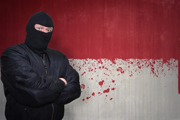 Farlig man i en mask stående nära en mur med målade nationella flaggan i Monaco — Stockfoto