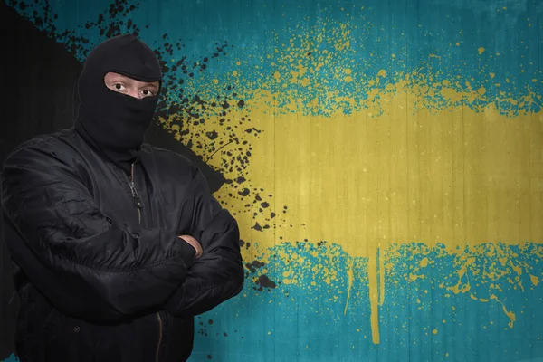 Uomo pericoloso in una maschera in piedi vicino a un muro con bandiera nazionale dipinta di Bahamas — Foto Stock