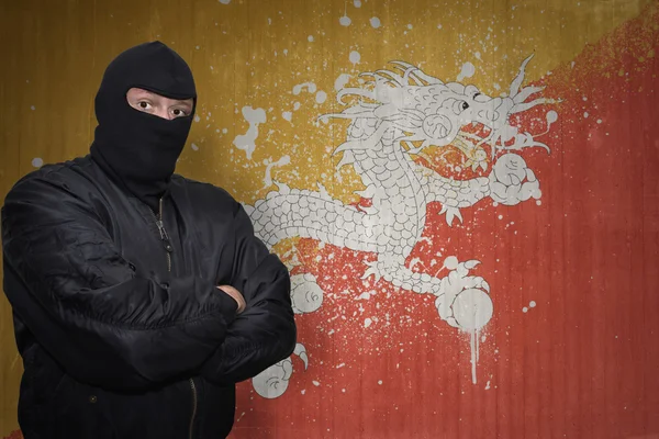 Niebezpieczny człowiek w maska stojący w pobliżu ściany malowane flaga Bhutanu — Zdjęcie stockowe
