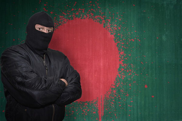 dangerous man in a mask standing near a wall with painted national flag of bangladesh