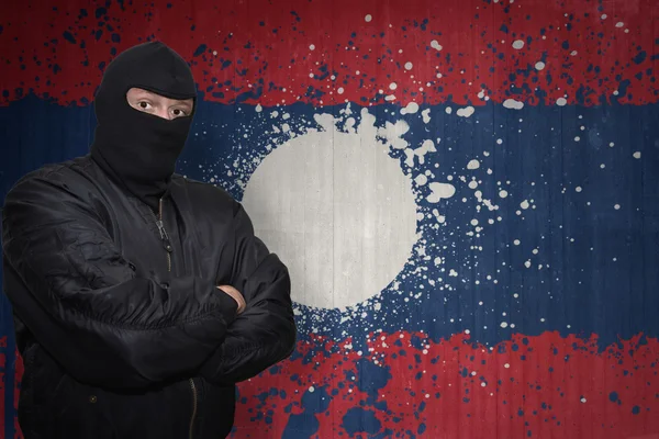 Uomo pericoloso in una maschera in piedi vicino a un muro con bandiera nazionale dipinta del Laos — Foto Stock
