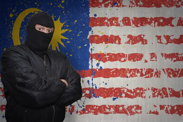 Опасный человек в маске, стоящий у стены с раскрашенным национальным флагом Малайзии — стоковое фото