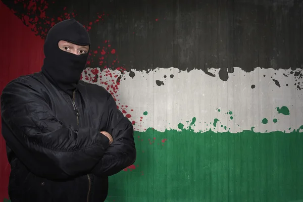 Homem perigoso em uma máscara que está perto de uma parede com bandeira nacional pintada de Palestina — Fotografia de Stock