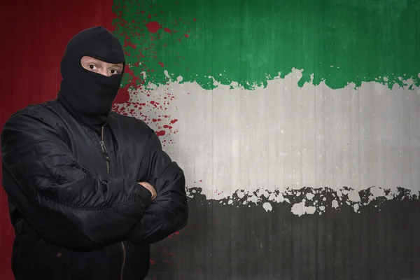 Homem perigoso em uma máscara que está perto de uma parede com a bandeira nacional pintada de emirados árabes unidos — Fotografia de Stock