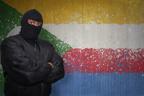 Dangerous man in a mask standing near a wall with painted national flag of comoros — Stock Photo, Image