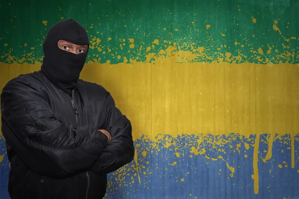 Опасный человек в маске, стоящий у стены с раскрашенным национальным флагом габона — стоковое фото