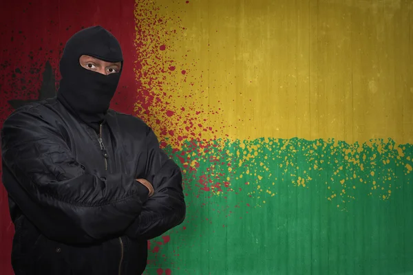 Homem perigoso em uma máscara que está perto de uma parede com a bandeira nacional pintada de bissau de Guiné — Fotografia de Stock