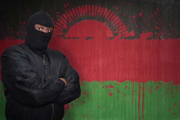 Uomo pericoloso in una maschera in piedi vicino a un muro con bandiera nazionale dipinta del Malawi — Foto Stock