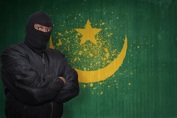 Uomo pericoloso in una maschera in piedi vicino a un muro con bandiera nazionale dipinta di mauritania — Foto Stock