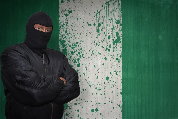 Homem perigoso em uma máscara que está perto de uma parede com a bandeira nacional pintada de nigeria — Fotografia de Stock