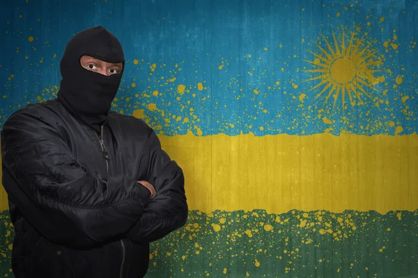 Опасный человек в маске, стоящий у стены с раскрашенным национальным флагом Руанды — стоковое фото