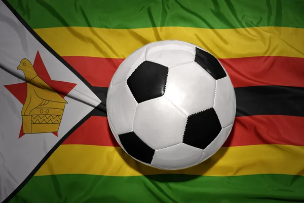 Bola de futebol preto e branco na bandeira nacional de zimbabwe — Fotografia de Stock