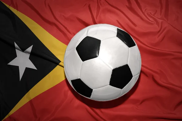 Bola de futebol preto e branco na bandeira nacional do timor leste — Fotografia de Stock