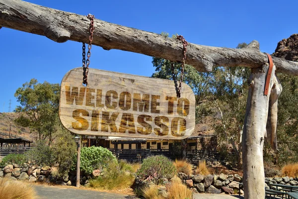 Vecchio cartello in legno vintage con il testo "Benvenuti a Sikasso" appeso ad un ramo — Foto Stock