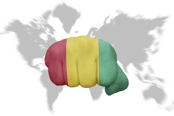 Pugno con la bandiera nazionale della Guinea su sfondo mappa del mondo — Foto Stock