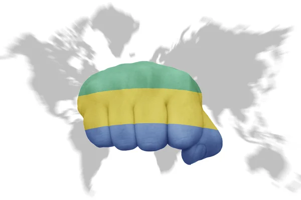 Vuist met de nationale vlag van gabon op een wereld kaart achtergrond — Stockfoto