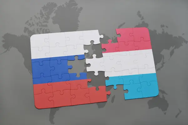 Puzzel met de nationale vlag van Rusland en Luxemburg op een wereld kaart achtergrond. — Stockfoto