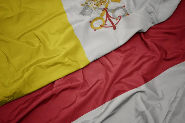waving colorful flag of indonesia and national flag of vatican city. macro