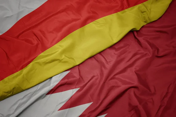 waving colorful flag of bahrain and national flag of south ossetia. macro