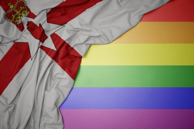 Eşcinsel gökkuşağı arka planında Kuzey İrlanda 'nın renkli ulusal bayrağını sallayarak.