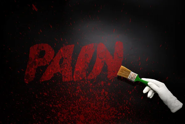 Hand in glove with the brush painting the text pain on a black surfacet — Stock Photo, Image