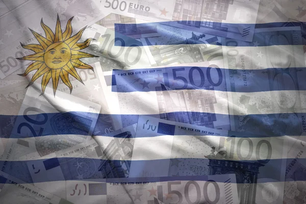 Colorido ondeando bandera uruguaya sobre un fondo de dinero en euros —  Fotos de Stock