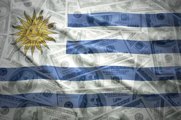 Colorido ondeando bandera uruguaya sobre un fondo de dinero en dólares americanos —  Fotos de Stock