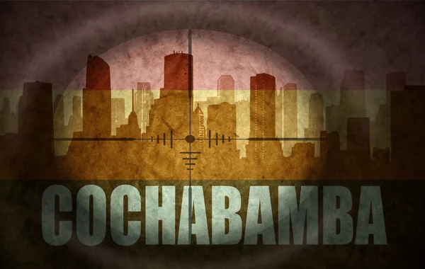 Снайперский прицел нацелен на абстрактный силуэт города с текстом Кочабамба под винтажным боливийским флагом. концепция — стоковое фото
