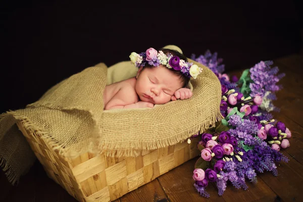 Bayi perempuan cantik yang baru lahir dengan karangan bunga ungu tidur di keranjang Wicker — Stok Foto