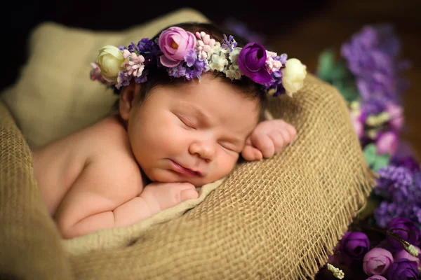 Beautiful newborn baby girl with a purple wreath sleeps in a wicker basket — Stock Photo, Image