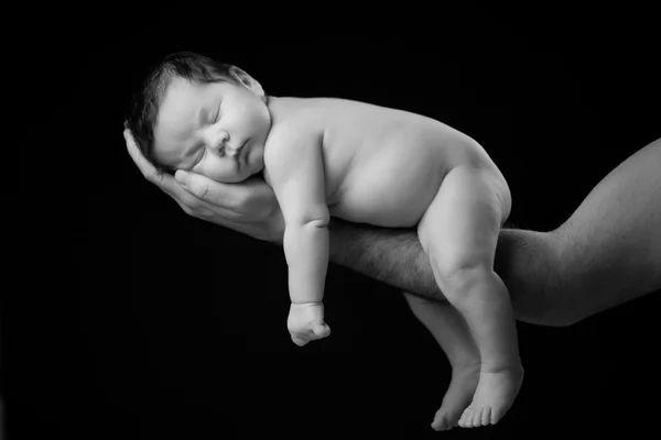 Nahaufnahme eines schlafenden Neugeborenen in den Händen des Vaters auf schwarzem Hintergrund — Stockfoto
