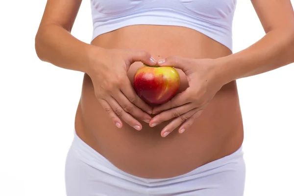 Close-up de uma barriga grávida e maçã. Mãos dobradas no coração. Em um fundo branco — Fotografia de Stock