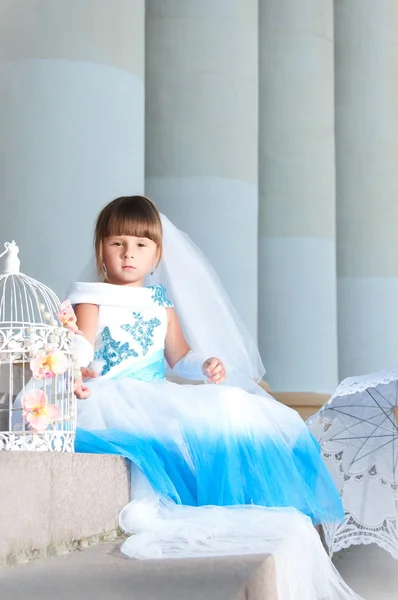 Маленька дівчинка моди в чудовій синьо-білій вечірній сукні сидить на сходах біля колонади — стокове фото